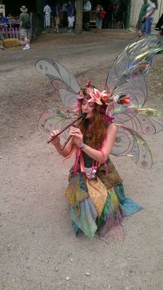 a woman dressed up as a fairy with wings and flowers on her head sitting in the dirt