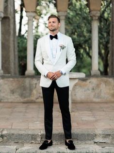 a man in a white tuxedo and bow tie is standing on some steps