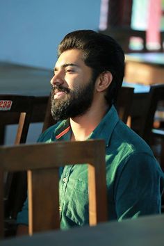 a man with a beard sitting in a chair and looking off to the side while smiling