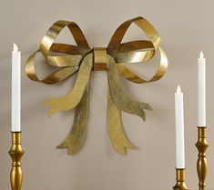 a gold bow is hanging on the wall next to two candles and a candle holder