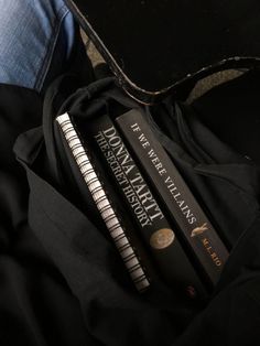 three books are sitting on top of a black bag and some jeans, one is folded over the other