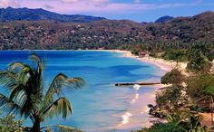 the beach is surrounded by palm trees and blue water with mountains in the back ground