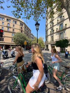 two women riding bikes down the street in front of buildings and people walking on the sidewalk