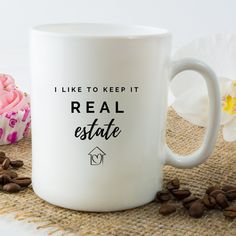 a white coffee mug with the words real estate on it next to some coffee beans