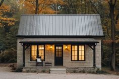 a small house with a metal roof and two windows on the front porch is lit up at night