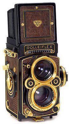 an old fashioned camera sitting on top of a white surface with gold trimmings