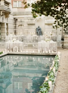 an outdoor wedding reception with candles and greenery around the pool in front of a building