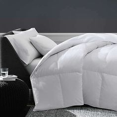 a white comforter sitting on top of a bed next to a night stand and lamp