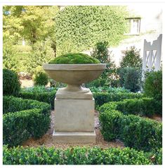 a large stone planter sitting in the middle of a garden surrounded by shrubbery