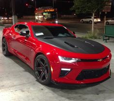 a red chevrolet camaro is parked in the parking lot at night with its hood up