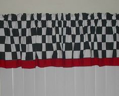 a black and white checkered window curtain with red trim on the bottom, in front of a radiator