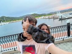 a man and woman taking a selfie in front of a lake with boats on the water