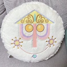 a white round pillow with a house on it's face and two circles in the center