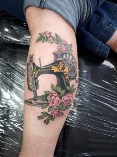 a tattoo on the leg of a person with a sewing machine and flowers around it