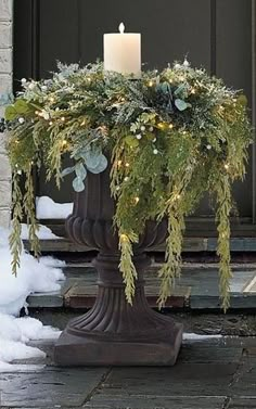 a candle that is on top of a planter with greenery and lights in it