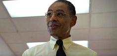 a man wearing glasses and a tie standing in a room with a white wall behind him