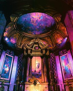 the inside of a church with paintings on the walls and ceiling, lit up by colorful lights