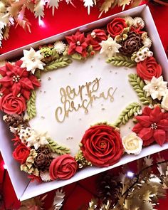 a christmas cake with red and white flowers in a box on top of tinsel