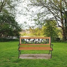 a wooden bench sitting on top of a lush green grass covered park field next to trees