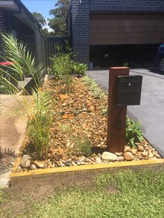 a mailbox sitting in the middle of a garden with rocks and plants around it