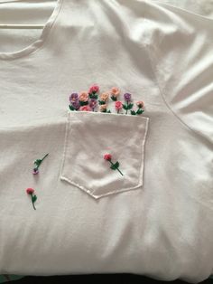 some pink and purple flowers are in the pocket of a white t - shirt that has been embroidered onto it