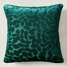 a green pillow with leaves on it against a white wall and the bottom part of the pillow is made from velvet