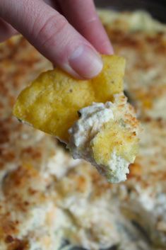 a hand holding up a piece of food over a pan filled with cheese and sauce