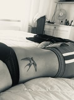 a woman laying on top of a bed with a bird tattoo on her leg and chest