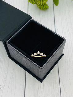 an open jewelry box on a white wooden floor with flowers in the background and a single diamond ring sitting inside it