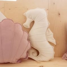 two decorative seahorses sitting on top of a wooden shelf next to pink and white pillows