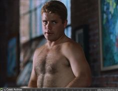 a man without a shirt standing in front of a brick wall and looking at the camera