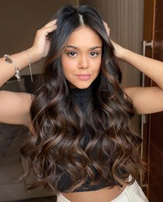 a woman with long dark brown hair is holding her hands on her head and looking at the camera