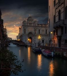 boats are parked on the water in front of an old building at night with lights reflecting off it's windows