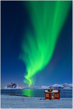 an aurora bore over a small house in the middle of snow covered ground with mountains in the background