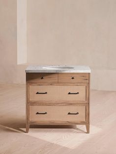 a bathroom vanity with two drawers and a white marble top on a wooden floor in front of a beige wall