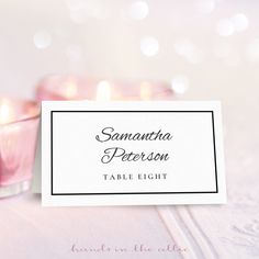 a place card sitting on top of a table next to a pink vase with candles in it