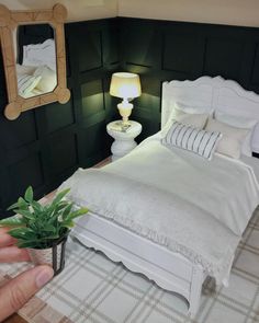 a person holding a small potted plant in front of a bed with white sheets and pillows