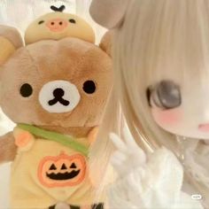 a teddy bear with an orange pumpkin on it's chest next to a doll