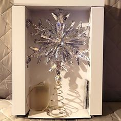 a snowflake in a white box on a bed with a cup and saucer