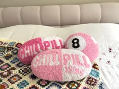 two pink pillows that are on top of a white bedspread with an eight ball in the middle