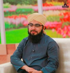 a man with a turban and glasses sitting on a couch in front of flowers