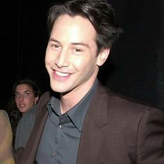 a man in a suit smiling at the camera while standing next to another man wearing a black shirt