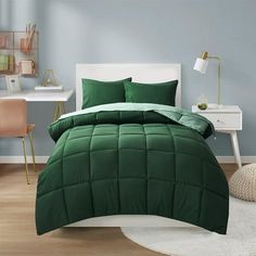 a bed with green comforter and pillows on top of it in front of a desk