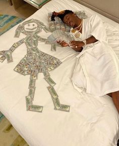 a woman laying on top of a white bed covered in paper money cut out figures