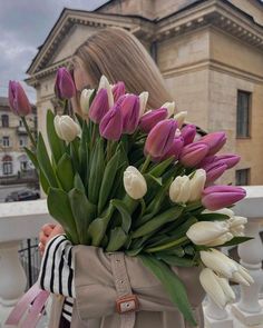 a woman is holding a bouquet of tulips in front of an old building