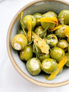 a bowl filled with green olives and orange peels covered in salt on top of a white table