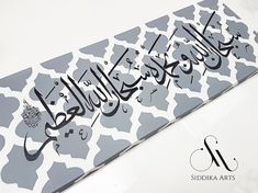 an arabic calligraphy is displayed on the side of a white and gray patterned paper