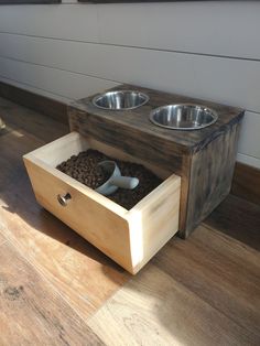 a wooden box with two bowls and spoons in it sitting on the floor next to a wall