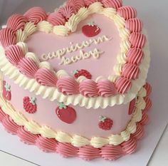 a pink heart shaped cake with white frosting and strawberries on the top is sitting on a table