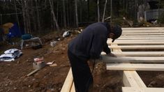 a man is working on some wooden beams in the woods with other items around him